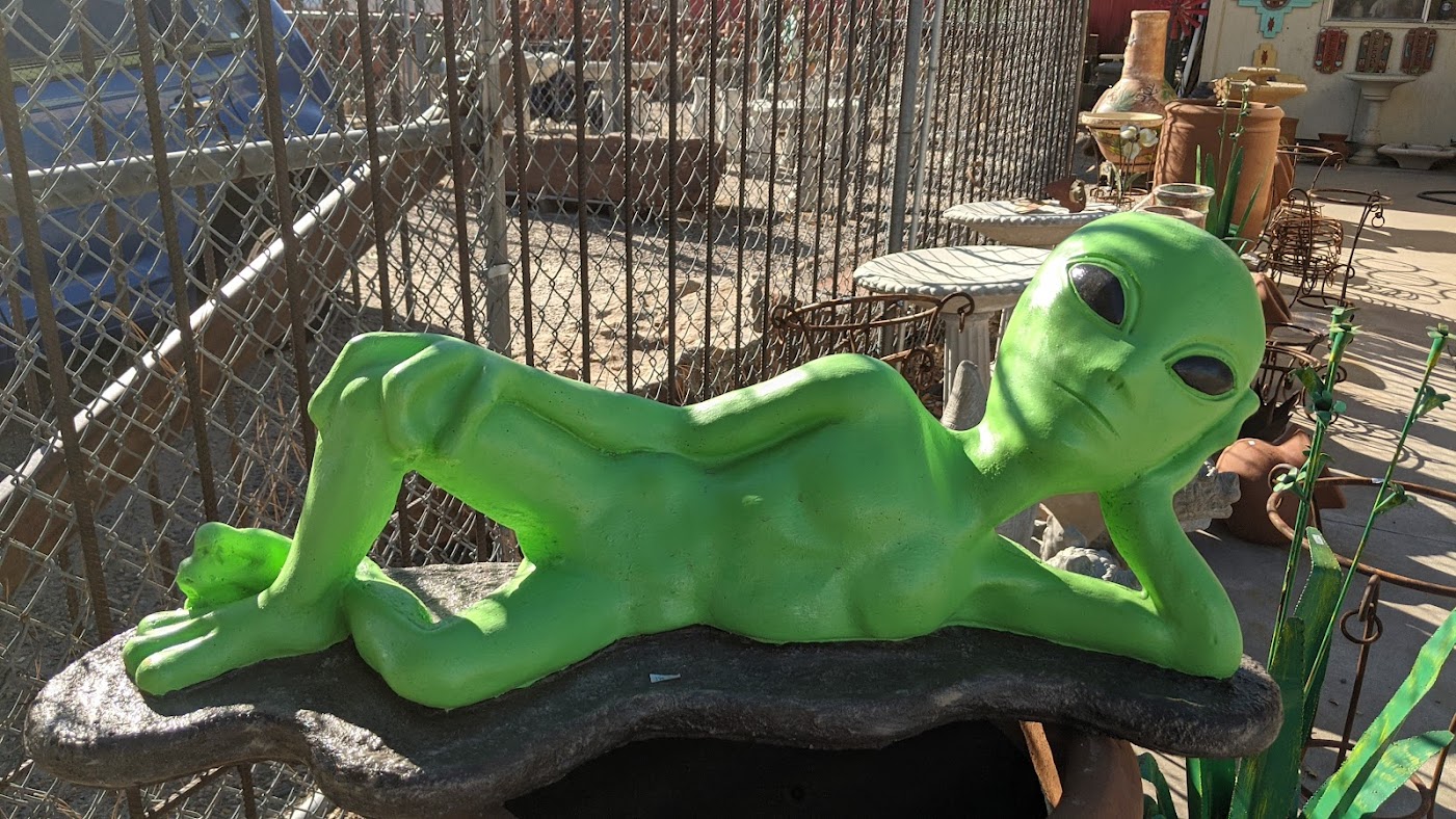 A garden statue of a bright green alien relaxing on the ground